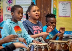 Three third grade students playing West African drums in classroom