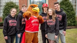 Quints wearing Montclair State University shirts and posing with Rocky mascot