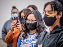 Two students in face masks watch a flag raising ceremony