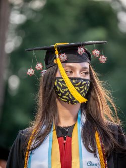 student at graduation wearing face mask and mortarboard decorated with coronavirus molecules