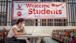 student at table with laptop with a banner on the wall behind her reading Welcome Back, Students