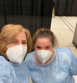 Associate Professors Marybeth Duffy and Courtney Reinisch in scrubs and masks at a vaccine center