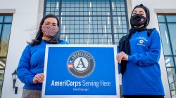 Two students outside with face masks holding AmeriCorps sign