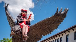 Graduate setting off confetti while sitting on Red Hawk statue