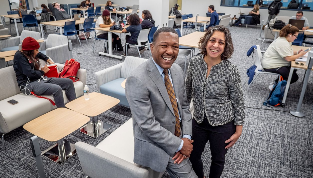 David Hood and Danielle Insalaco-Egan posing on furniture in student-filled lounge