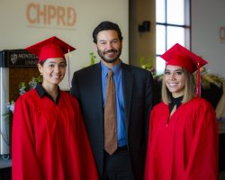 President Koppell posing with two students in red graduate school regalia