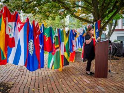 Katia Paz Goldfarb speaks at a podium in front of a clothesline strung with flags