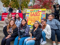 Members of the Latin American Student Organization seated around a painted posterboard with the club's name