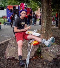 Student with broken leg rests on a boulder to eat lunch