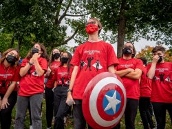 Group of student volunteers in matching red tee shirts, one carrying a Captain America shield