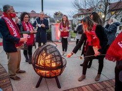 Faculty and staff wearing red scarves gather around a fire pit to make s'mores at Montclair State University