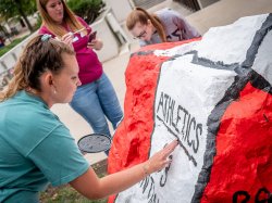 Student touching up the MSU Athletics rock