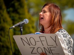 Woman speaking into microphone holding sign that reads 'no fly zone'