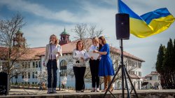 Four women on stage speaking into the micrphone under ukranian flag