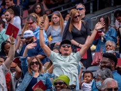 Photo of a man with raised arms cheering on graduates in a crowded stadium