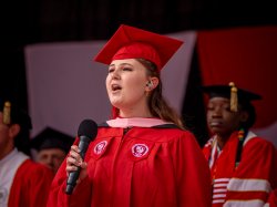 Photo of Lisa Bremer in her red graduation robes singing the National Anthem