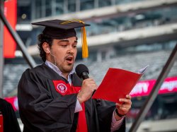 Photo of Alec Lobein his red graduation robes singing the Alma Mater.