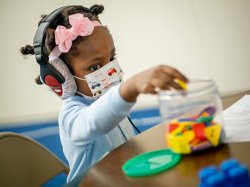 child with headphones placing blocks in bucket