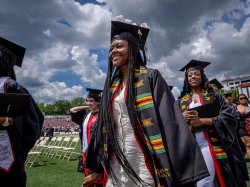 Photo of a graduate walking towards a stage with a blue sky and cloouds overhead