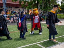 Photo of Rocky the Red Hawk giving a high-five to a student at convocation