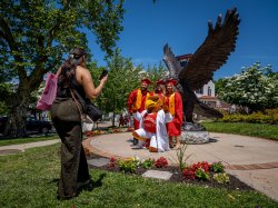 photo of students in graduation robes posing in front of a red hawk statue