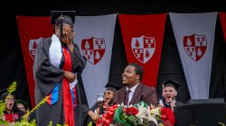 Man in cap and gown on stage proposing to woman in cap and gown