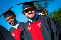 photo of a graduate in red and black robes wearing sunglasses and smiling