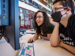 Two students looking closely at monitor over colored video editing keyboard