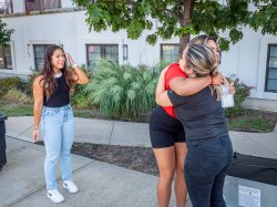 two people hug as another looks on