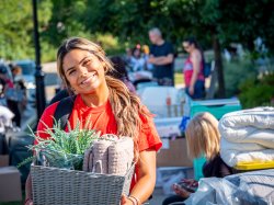 student smiles for the camera, holding a basket with towels and a plant