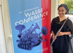 Karina Bloom holding a flute next to a banner reading Wasbe Conference