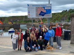group of students and faculty pose in front of Stonehaven Harbour