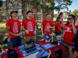 Four students at table on quad wearing red shirts