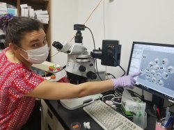 Ceren Citak sits in front of a microscope and points to a computer monitor