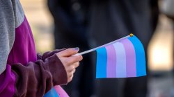 Close up of hands holding a small blue, pink and white transgender awareness flag.