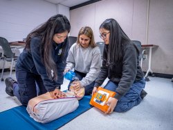 Three women practice CPR on a manikin.