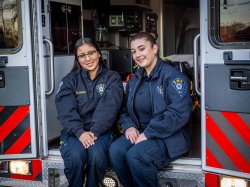 two women sit on the back of an ambulance.
