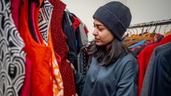 Student in winter cap peruses rack of dresses