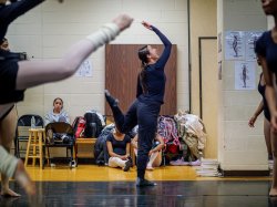 A female dancer with an arm and leg raised teaches a dance.
