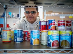 A male student peers through a shelf of canned food