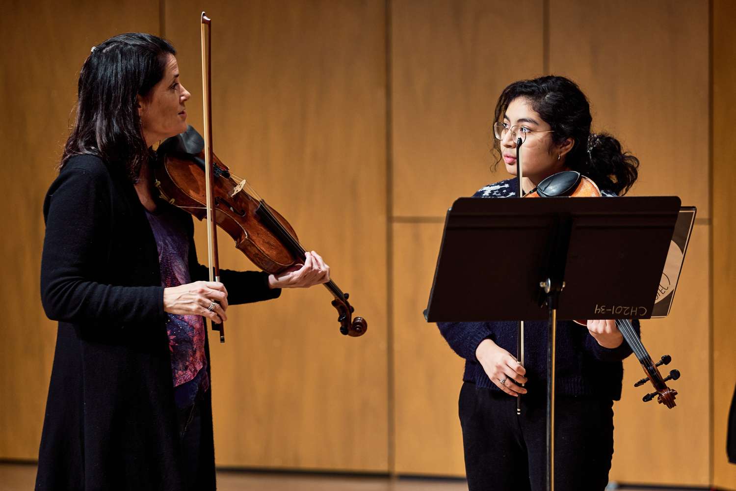 Female student playing violin listens to female instructor.