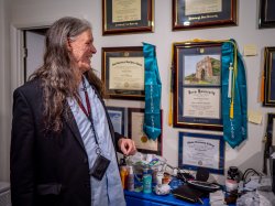 A smiling man looks at one of many diplomas on the wall.