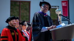 A man in academic regalia speaks at a podium.