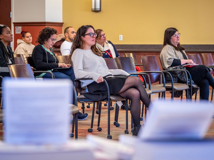 An audience of mostly women and one man sit, listening to a speaker.