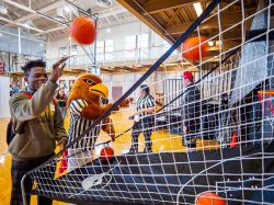 Male student shoots basketball alongside college mascot.