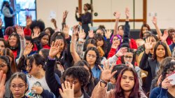 A large group of female students raise their hands in the air.