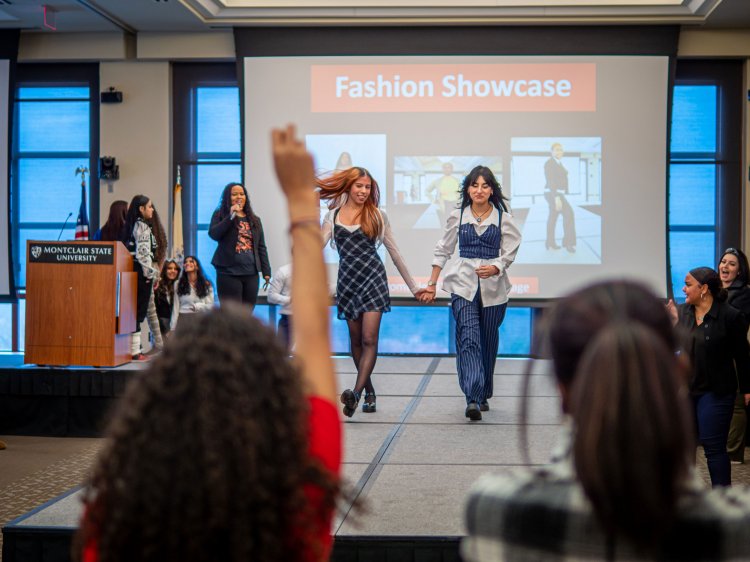 Two female students walk down a runway holding hands.