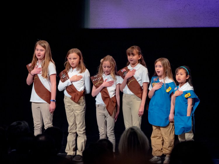 Six girls on stage with hands over their hearts.