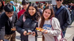 Two female students smile as they hold plates of food at an outdoor event.