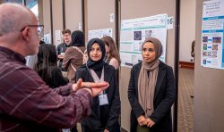 A man talks to two students in hijab about their research poster about annotating the genomes of sea phages.